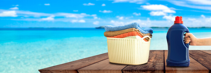 Laundry detergent bottle and basket stack of clean bath towels on wooden board in front of beach 