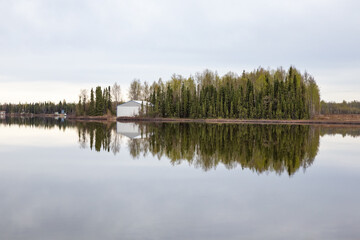 Boathouse and trees on shore reflecting in still Kashwitna Lake, Alaska
