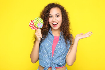 Surprised american girl holding colorful lollipops on yellow background