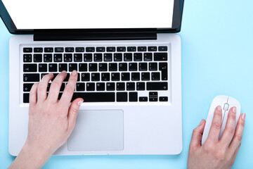 Female hands typing on laptop keyboard and using mouse on blue background