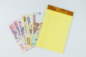 Many new banknotes Ukrainian hryvnia on yellow notebook on white background