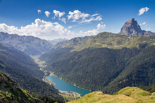 view of a valley in the pyrenees with a lake in the background and a rocky peak on the right on a summer day, lake of Fabregues and peak d'Ossau in the d'Ossau valley, Artouste, France