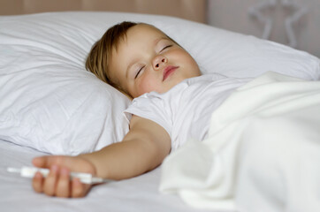 A small child's hand with a thermometer in bed. Selective focus. Sick infant toddler with a thermometer