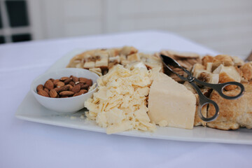 Cheese board on white platter with parmesan, crackers, bread and almonds