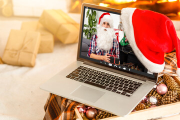 Computer in cozy room with hanging red hat and with Santa Claus on screen wishing Merry Christmas and Happy New Year online