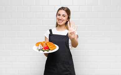 blonde pretty woman smiling and looking friendly, showing number four or fourth with hand forward,...