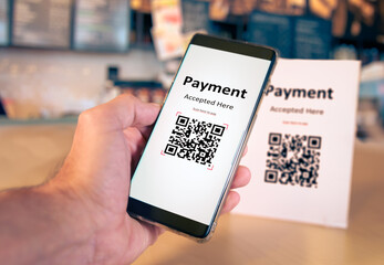 Qr code payment or cashless technology concept. Coffee shop accepting digital pay without money . Plastic tag on table and hand using mobile phone application to scan qr code
