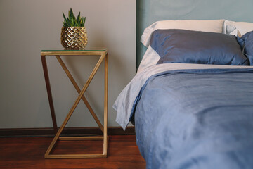 Golden luxury metal bedside table with vase in bedroom with dark blue textile