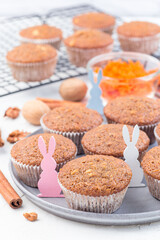 Carrot cake muffins with walnuts on gray plate and cooling rack, decorated with wooden Easter bunnies, vertical