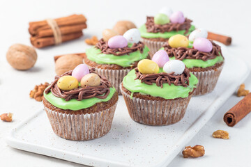 Carrot cake muffins with cream cheese frosting and Easter chocolate eggs, on white plate, horizontal