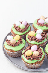 Carrot cake muffins with cream cheese frosting and Easter chocolate eggs, on gray plate, vertical closeup, copy space