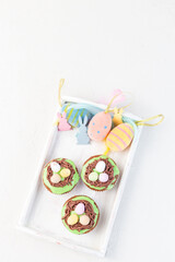 Easter carrot cake muffins with cream cheese frosting and chocolate eggs, on white wooden tray with Easter eggs, bunnies and feathers, vertical, copy space, top view