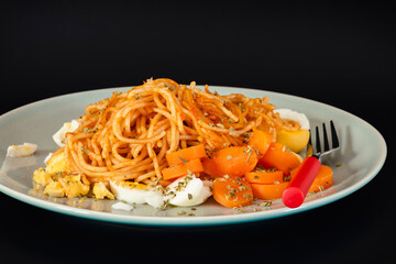 Espaguetis con tomate, huevo, zanahoria y perejil, sobre fondo negro