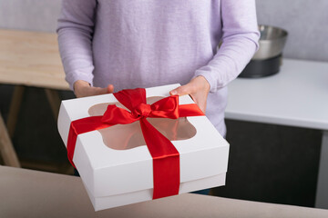 White gift box with red bow in female hands. Close up