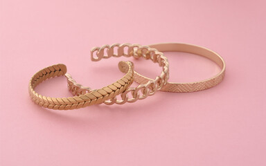 Three modern golden bracelets layed on pink background