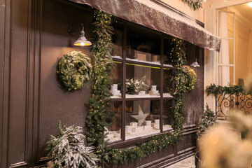 Fototapeta na wymiar Vintage street cafe window. French cafeteria showcase with Christmas fir wreath covered with snow. Facade of street retro restaurant. Winter cafe decoration. Copy space. Christmas concept. Postcard