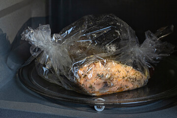 Spiced fresh trout fish wrapped in a baking sleeve in a microvawe oven, cooked, closeup view