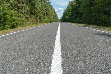Fototapeta na wymiar Empty asphalt road through woods and fields. New fresh asphalt pavement away from the city. Development of rural infrastructure. Road marking lines close up.