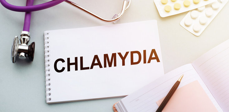 Stethoscope, pills and notebook with CHLAMYDIA word on medical desk.