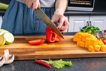 Preparing for home party. Woman cuts pepper on cutting board.