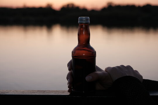 beer bottle in front of sunset hlded by the hand.
