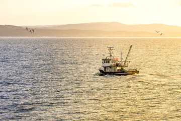 The fishing boat is returning to the harbor at sunset.
