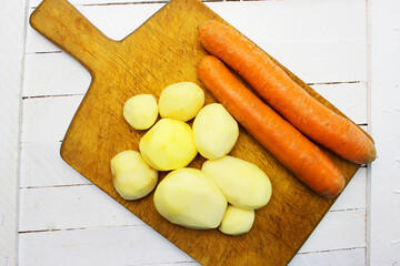 peeled round potatoes a huge pile of very large fresh and sweet carrots on a white wooden table. beautiful fresh market organic carrots in a large pile close-up full frame healthy food and healthy