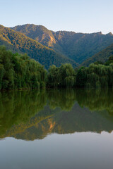 Beautiful summer landscape in the mountains: mountain lake, mountain slopes in green trees, reflection of mountains and trees in the lake water