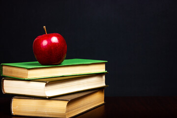 A stack of books and a red apple on a dark background. School, student education.