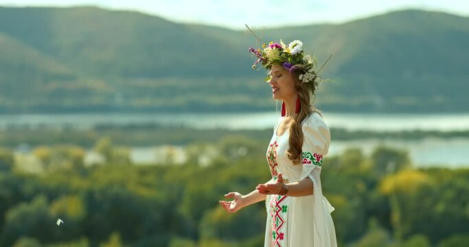 Portrait, a young beautiful woman in a folk costume and with a floral wreath on her head sings songs in nature. Traditions and customs of the Slavic peoples. 4k, ProRes