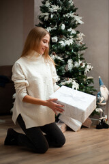 Beautiful woman dressed in a white sweater with gifts near the Christmas tree