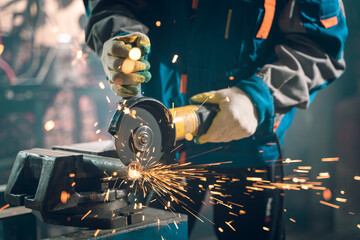 Locksmith in special clothes and goggles works in production. Metal processing with angle grinder. Sparks in metalworking