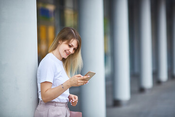 Young woman smiles and holds in her hands and looks at the smartphone.