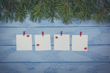 Christmas or New Year mock up: some pine branches and white stickers with small red hearts and clothespins on the blue boards