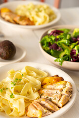 Delicious hearty dinner or lunch, pasta with stewed chicken breast and avocado and greens salad on a white wooden table