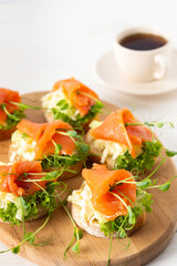 Obraz na płótnie Canvas Canapes with mozzarella cheese, salad, salmon and pea sprouts, toast with red fish on a wooden board close up