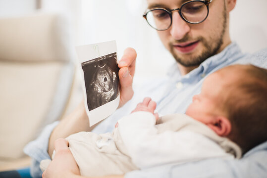 A man with a newborn baby showing an ultrasound picture, father moment with a baby