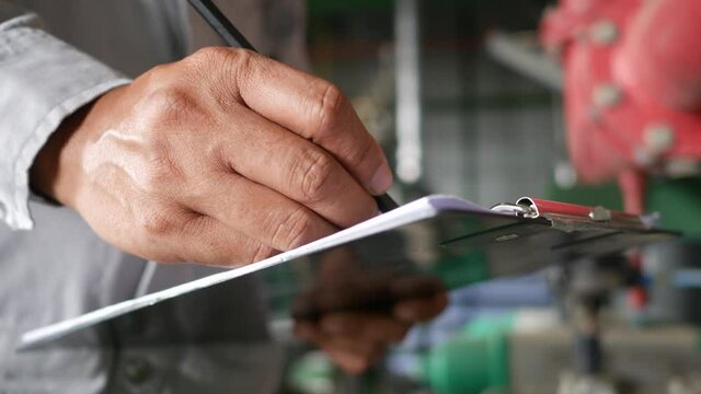 An employee holding a clipboard examining something in an industrial plant and recording the results on a paper sheet.