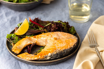 Fried salmon steak with salad in a plate close-up, white wine in a glass, delicious hearty dinner or lunch