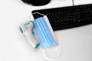 Non-contact thermometer and medical mask on a keyboard background in the office
