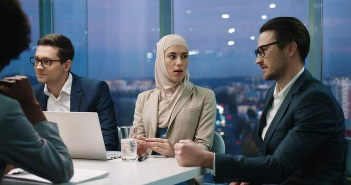 Portrait of young multi ethnic entrepreneurs sitting in modern office at team meeting and speaking. Caucasian man discussing business ideas with Muslim woman at business conference. Job concept