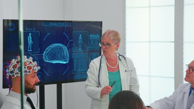 Brainwave electroencephalograph examination in hospital brainstorming office by medical physician. Monitor shows modern brain study while team of scientist adjusts the device.