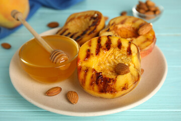 Delicious grilled peaches with honey and almonds on light blue wooden table, closeup