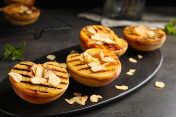 Delicious grilled peaches with almond flakes on grey table