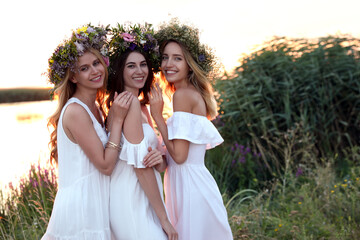 Fototapeta na wymiar Young women wearing wreaths made of beautiful flowers outdoors at sunset