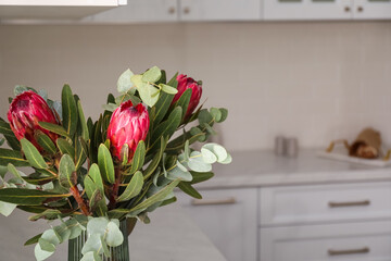 Bouquet of beautiful protea flowers and eucalyptus branches in kitchen interior, closeup. Space for text