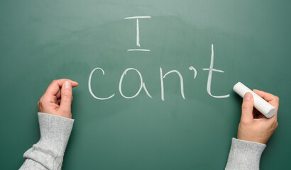 woman's hand writes on a green chalk board with white chalk i cant