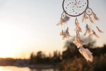 Beautiful handmade dream catcher near river on sunny day. Space for text