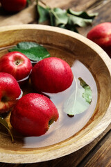 Ripe red apples in bowl of water on wooden table, closeup