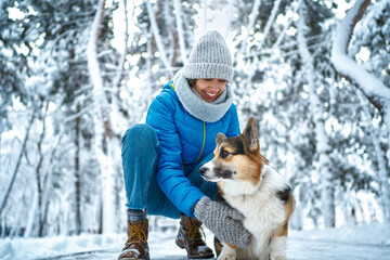 Woman stroking her fluffy cute pet Welsh Corgi puppy in winter landscape. Idyllic winter holidays with dog. Focus on dog